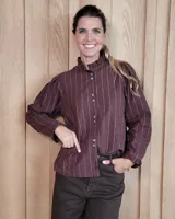 Camisa de manga larga con estampado de rayas verticales en tonos crudo y beige. Presenta cuello alto con volados, cierre frontal con botones dobles y puños con volados.