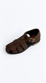 Sandalias cangrejeras de gamuza color marrón, con punta redonda, taco bajo, talonera cerrada y tira con hebilla metálica ajustable en el tobillo.