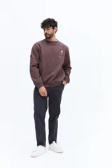 Buzo de algodón color marrón oscuro (ciruela/ciruela quemado) con cuello redondo, puños y ruedo acanalados. Presenta un pequeño bordado de motivos florales en el pecho.