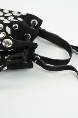Cartera tipo bucket bag de gamuza negra, decorada con múltiples tachas metálicas plateadas de forma circular. Cuenta con cierre de cordón ajustable y asa superior.