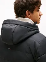 Campera acolchada de color negro confeccionada en tejido ripstop de nailon con acabado repelente al agua. Presenta un diseño con relleno térmico, capucha fija ajustable con cordón, cierre frontal de cremallera y bolsillos laterales con cierre. Incluye el logo de Tommy Hilfiger bordado en el pecho.