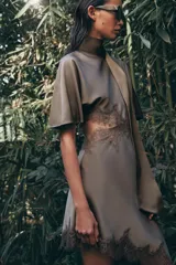 Vestido midi satinado de cuello subido y manga corta tipo capa. Presenta aberturas laterales con aplicación de encaje a tono y bajo asimétrico con detalle de encaje. Incluye un pañuelo integrado en el mismo tejido y cierre posterior con botones forrados.