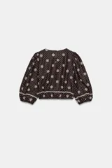 Blusa azul marino con estampado de lunares blancos, cuello redondo y mangas abullonadas. Presenta detalles de bordados perforados, volantes delanteros y acabados elásticos.