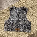 Chaleco sin mangas de cuero con estampado de piel de serpiente en tonos grises y negros. Presenta un corte recto y una etiqueta de cuero marrón con la marca Ecuestre en la parte inferior.