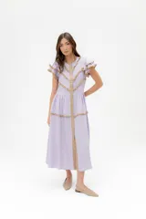 Vestido midi de lino blanco con diseño de broderie, cuello alto, cierre frontal con botones y volados decorativos en los hombros y el cuerpo.