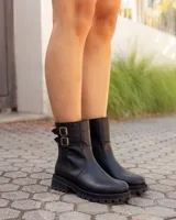 Botas de caña media en cuero negro, con suela track gruesa y dos correas laterales con hebillas metálicas doradas.