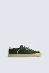 Zapatilla deportiva de estilo retro con diseño de paneles en cuero sintético color verde oscuro, detalles en crema y suela de goma en contraste.