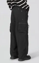 Pantalón cargo oversize de textil técnico color negro, con silueta relajada y múltiples bolsillos laterales de gran tamaño con cierres metálicos. Incluye cinturón integrado de cinta de seguridad con hebilla de encastre técnica.