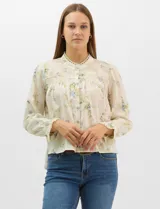 Blusa de algodón con estampado floral de flores silvestres sobre fondo claro. Presenta cuello redondo con detalle de puntilla, abotonadura frontal, canesú con frunces y mangas largas con puños elásticos decorados con puntilla.