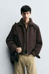 Cazadora cropped fit color marrón oscuro, confeccionada en tejido de algodón. Presenta cuello solapa, manga larga con puño abotonado, bolsillos de vivo en la cadera y un bolsillo interior. El bajo tiene elástico en la espalda y el cierre es frontal con cremallera.