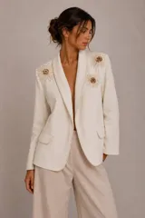 Blazer color beige con solapas tipo chal, bolsillos delanteros de ribete y apliques de margaritas de crochet bordadas con cuentas en los hombros.
