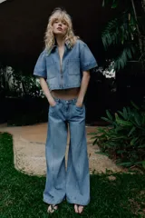 Jeans de tiro alto con pernera ancha y costuras marcadas en el frente. Presenta cintura elástica en la parte posterior, cierre frontal con cremallera y botón, bolsillos delanteros y bolsillos de plastrón en la parte trasera.