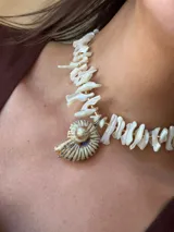 Collar corto con cuentas irregulares de nácar color blanco y dije de caracol con detalles dorados. Cierre con gancho y cadena de acero quirúrgico para regular el largo.