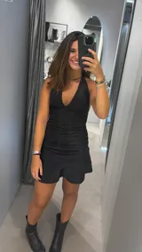 Vestido corto negro con brillo, escote en V profundo y cuello halter. La falda tiene un pequeño volante en el ruedo.