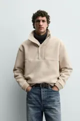 Sudadera de corte relajado confeccionada en tejido con textura de borreguillo, con cuello subido y cierre frontal de botones a presión. Presenta puños y ruedo con acabado en rib.