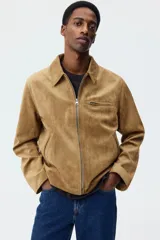 Campera de gamuza sintética color tostado, con cuello camisero, cierre frontal, bolsillo superior con cierre y bolsillos laterales ribeteados.