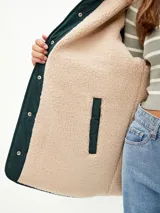 Campera acolchada de color verde oscuro con diseño matelasseado, interior forrado en corderito sintético color beige, con capucha y cierre frontal de botones a presión.