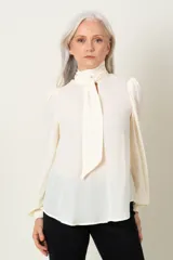 Blusa color marfil de manga larga con frunce en hombros y puños, escote en V con lazo y cierre de puños con dos botones.