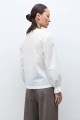 Remera de color blanco con cuello redondo y mangas largas abullonadas que presentan puños con volados.