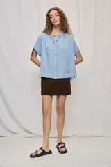 Camisa de manga corta color celeste, confeccionada en viscosa fluida, con silueta amplia y escote redondo con frunces y lazo para anudar.