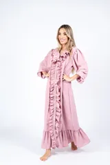 Vestido largo color crudo, estilo camisero, con cuello en V y volados verticales en el frente. Tiene mangas largas abullonadas y corte amplio.