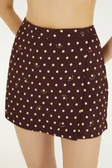 Falda pantalón corta de silueta recta en color marrón con estampado de lunares blancos y detalles sutiles de la marca. Presenta un diseño cruzado en el frente y cierre lateral con botón.
