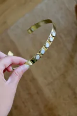 Gargantilla rígida de bronce dorado con incrustaciones de piedras blancas. Se ajusta a presión al cuello.