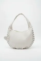 Cartera tipo hobo bag color blanco, con asa de hombro y detalles de tachas plateadas en los bordes. Incluye un charm colgante en forma de corazón con tachas.