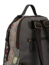 Mochila de tela color gris oscuro con diseño patchwork en los laterales y bordado floral en el frente. Incluye un llavero decorativo con borlas y cuentas, cierre principal, y logo de la marca en la parte superior.
