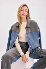 Campera de jean con diseño bicolor, combinando paneles en color gris oscuro y azul denim. Presenta cuello camisero, cierre frontal con botones metálicos y corte holgado.