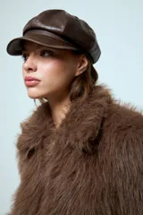 Boina estilo cap con visera, confeccionada en cuero vegano de color marrón oscuro. Presenta un diseño estructurado con costuras visibles en la parte superior.