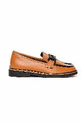 Mocasín de cuero color marrón claro, con detalles en negro en el borde superior y suela plana del mismo color. Cuenta con un adorno de cadena plástica negra en el empeine.