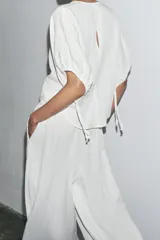 Pantalón palazzo color blanco, confeccionado en tejido de lyocell, de tiro medio, cintura elástica ajustable con cordones, bolsillos laterales ocultos y pierna ancha.