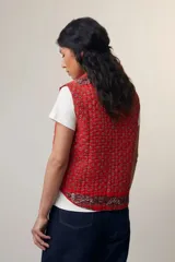 Chaleco sin mangas de algodón acolchado con estampado floral en tonos rojos y marrones. Tiene cuello camisero, cierre frontal con botones de madera y bolsillos de parche. El modelo Patchwork Tomette está tejido a mano.