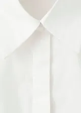 Camisa de popelín blanco entallada, con cuello camisero, mangas largas y cierre frontal de botones ocultos.