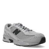 Championes New Balance modelo 509, color gris claro con detalles en gris oscuro y negro. Presentan una combinación de malla transpirable y superposiciones de gamuza. El logo 'N' lateral es negro.