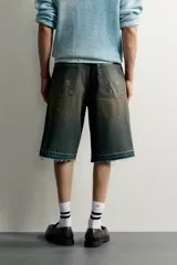 Bermuda de denim de algodón con efecto lavado desgastado en tonos marrones y azules. Tiene tiro medio, diseño de cinco bolsillos, pierna recta de corte holgado y bajo con acabado irregular. Cuenta con cierre frontal de cremallera y botón metálico.