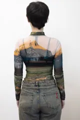 Remera crop top de mangas largas y cuello alto, confeccionada en tejido de red transparente con estampado de paisaje montañoso.