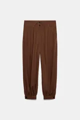 Pantalón de tiro alto color marrón, con diseño bombacho, bolsillos delanteros y puños ajustados con botón en el bajo. Cierre frontal con cremallera y botones.