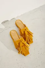 Zueco plano de cuero color dorado, con diseño de tiras anchas entrelazadas en el empeine y punta cuadrada.