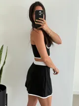 Conjunto deportivo negro con detalles en blanco, compuesto por un top corto con tirantes finos y una minifalda con short incorporado y abertura lateral.