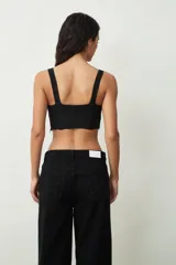 Top negro ajustado al cuerpo con escote en V profundo y tirantes anchos. Presenta un tejido texturizado, posiblemente encaje o jacquard, con un corte estilo corsé en la parte inferior.