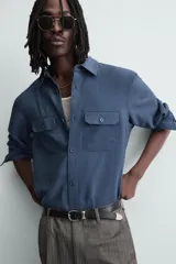 Camisa de corte relajado confeccionada en tejido con mezcla de viscosa. Presenta cuello solapa, manga larga con puños abotonados, bolsillos de plastrón con solapa en el pecho y cierre frontal de botones.