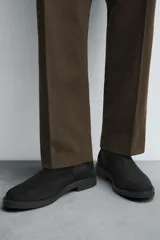 Bota estilo Chelsea de hombre, confeccionada en piel con acabado de serraje en color marrón. Presenta elásticos laterales oscuros para facilitar el calce, horma redonda y suela a tono con un ligero tacón.