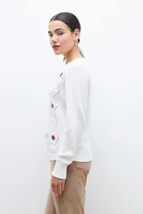 Sweater blanco de punto con bordado de flores azules, rojas y blancas. Tiene cuello redondo y mangas largas.