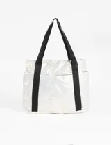 Bolso tipo tote bag metalizado color blanco, con diseño acolchado y pespuntes. Tiene doble asa de hombro, bolsillos laterales y cierre principal.