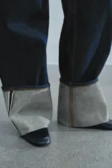 Jeans de tiro bajo y pernera ancha, confeccionados en denim azul oscuro con pespuntes en contraste. Cuentan con un diseño de cinco bolsillos, cierre frontal con cremallera y botón metálico, y destacan por su amplio doblando en el bajo que deja ver el revés de la tela con detalles de costura selvedge.