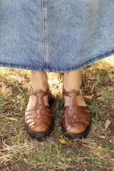 Sandalias de cuero color negro, tipo cangrejera, con diseño de tiras entrelazadas, tira en T, hebilla de ajuste en el tobillo, suela track y tacón cuadrado de madera.