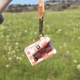 Billetera elástica de tejido resistente en tonos coral y rosado, con diseño de bloques geométricos verticales y argolla metálica lateral.