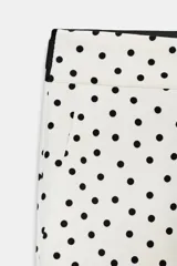 Pantalón blanco con estampado de lunares negros, de tiro medio con cintura elástica en la espalda, bolsillos delanteros y falsos bolsillos de vivo en la espalda. Bajo acabado con aberturas laterales y cierre frontal con cremallera, botón interior y gancho.